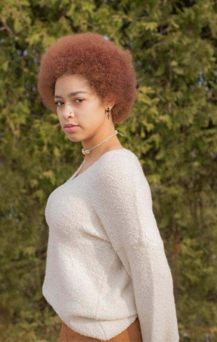 A Young Woman With Afro Hair Standing In A Field.