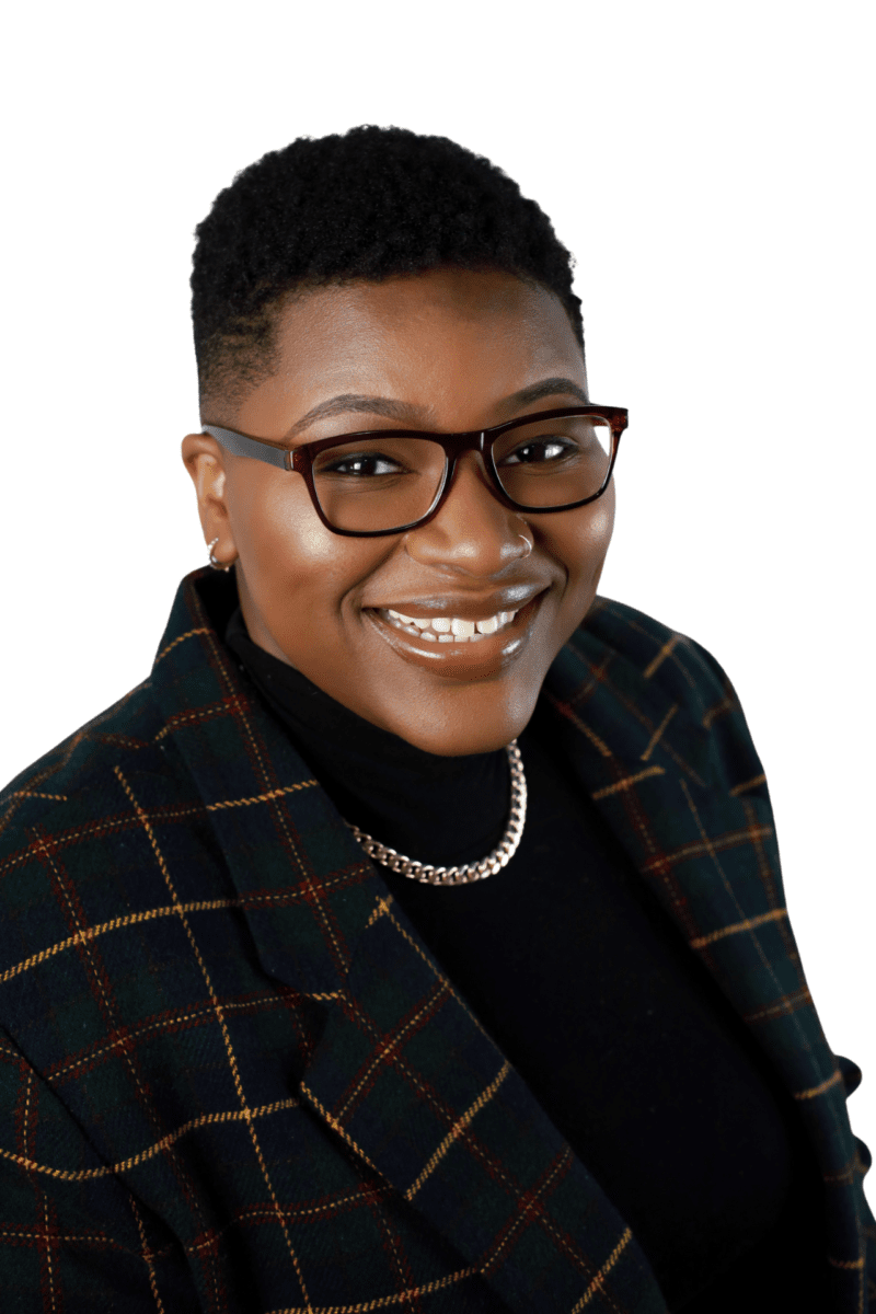 A Black Woman Wearing Glasses And A Plaid Jacket.