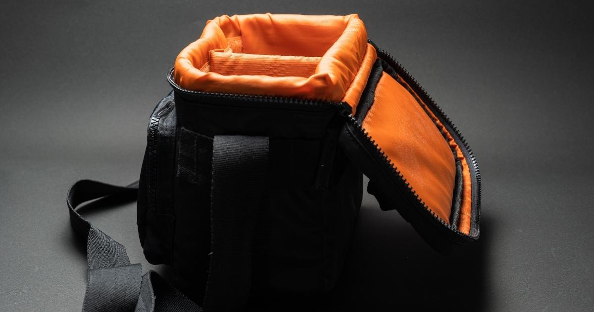 A Camera Bag With Orange And Black Design Placed On A Black Surface, Representing Photography.