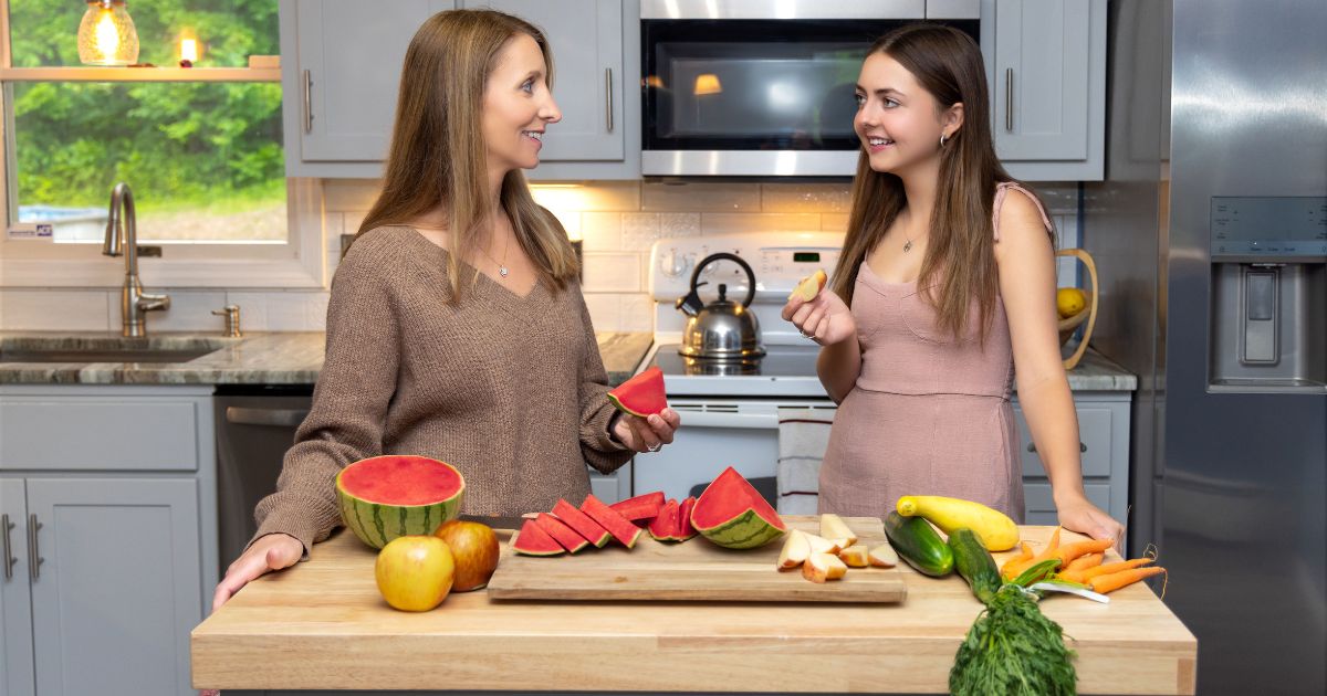Two Women Cooking At Home In Front Of A Cutting Board.