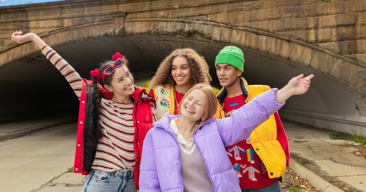 A Group Of Young People Standing In Front Of A Tunnel Wearing A Lot Of Colorful Clothes That Doesn'T Match One Another.