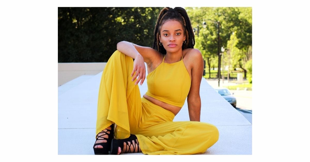 A Woman Poses For A Picture On A Wall In A Yellow Jumpsuit.