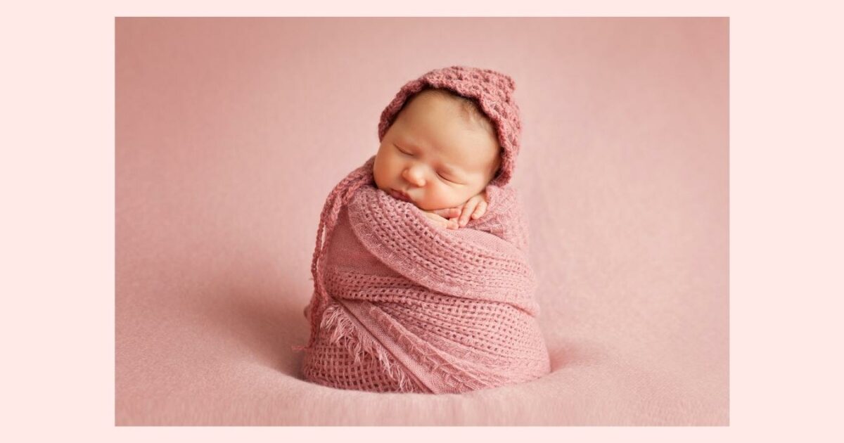 A Newborn Baby Wrapped In A Pink Blanket For A Photoshoot On A Pink Background.