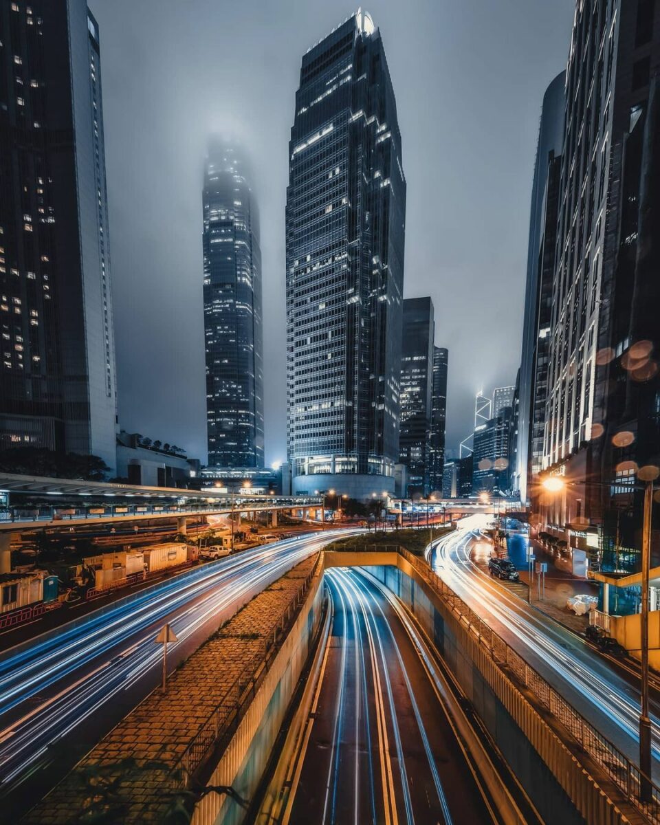 Captivating Hong Kong Cityscape At Night Illuminated By Speeding Car Lights, Showcasing The Art Of Capturing Motion Through The Optimal Use Of Shutter Speed In Photography.