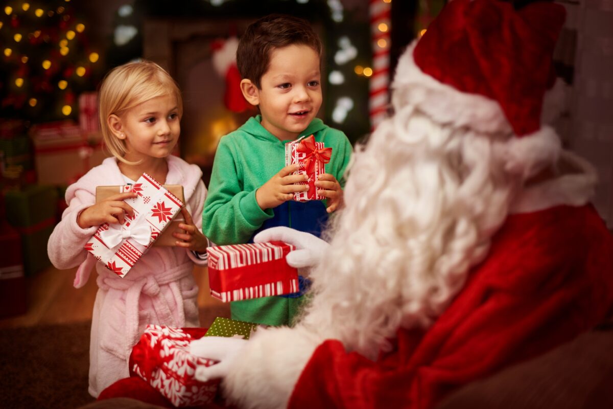 Santa Claus With Two Children Posing For A Santa Photoshoot, Holding Presents.
