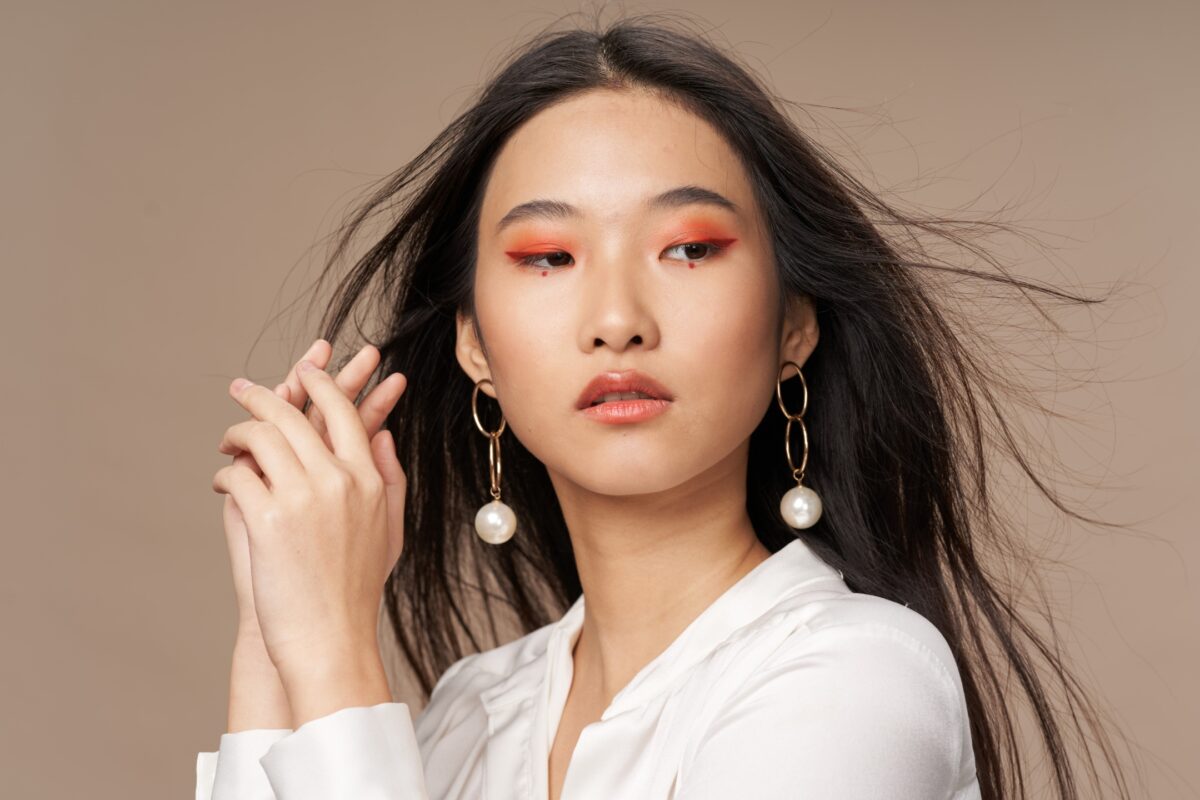 A Young Asian Woman In A White Shirt With Orange Earrings Poses For A Photo Session, While The Photographer Provides Posing Prompts And Guides On What To Say To Clients.