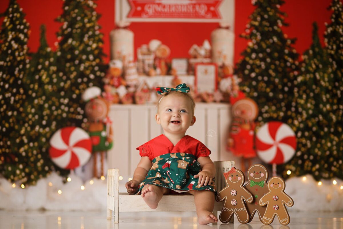 A Baby Girl Enjoying Christmas Mini Sessions On A Bench Surrounded By Festive Decorations.