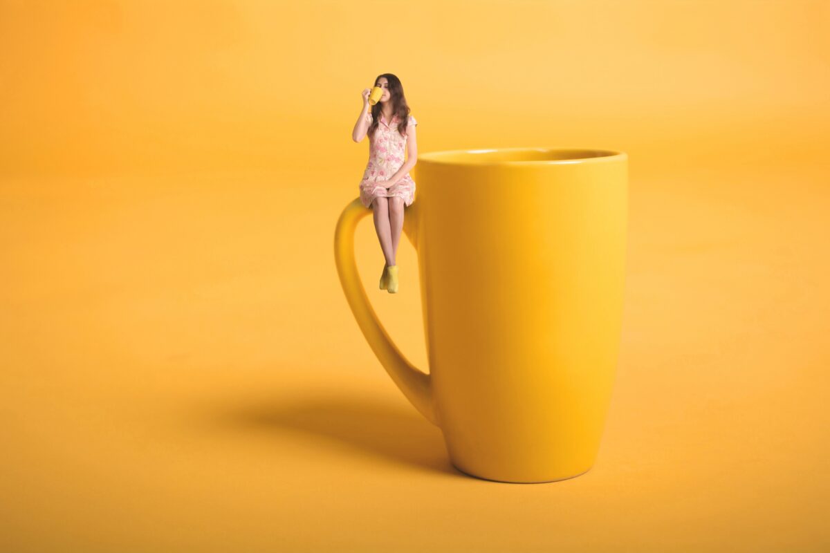        A Girl Sitting On Top Of A Yellow Coffee Cup While Turning Photos Into Art.