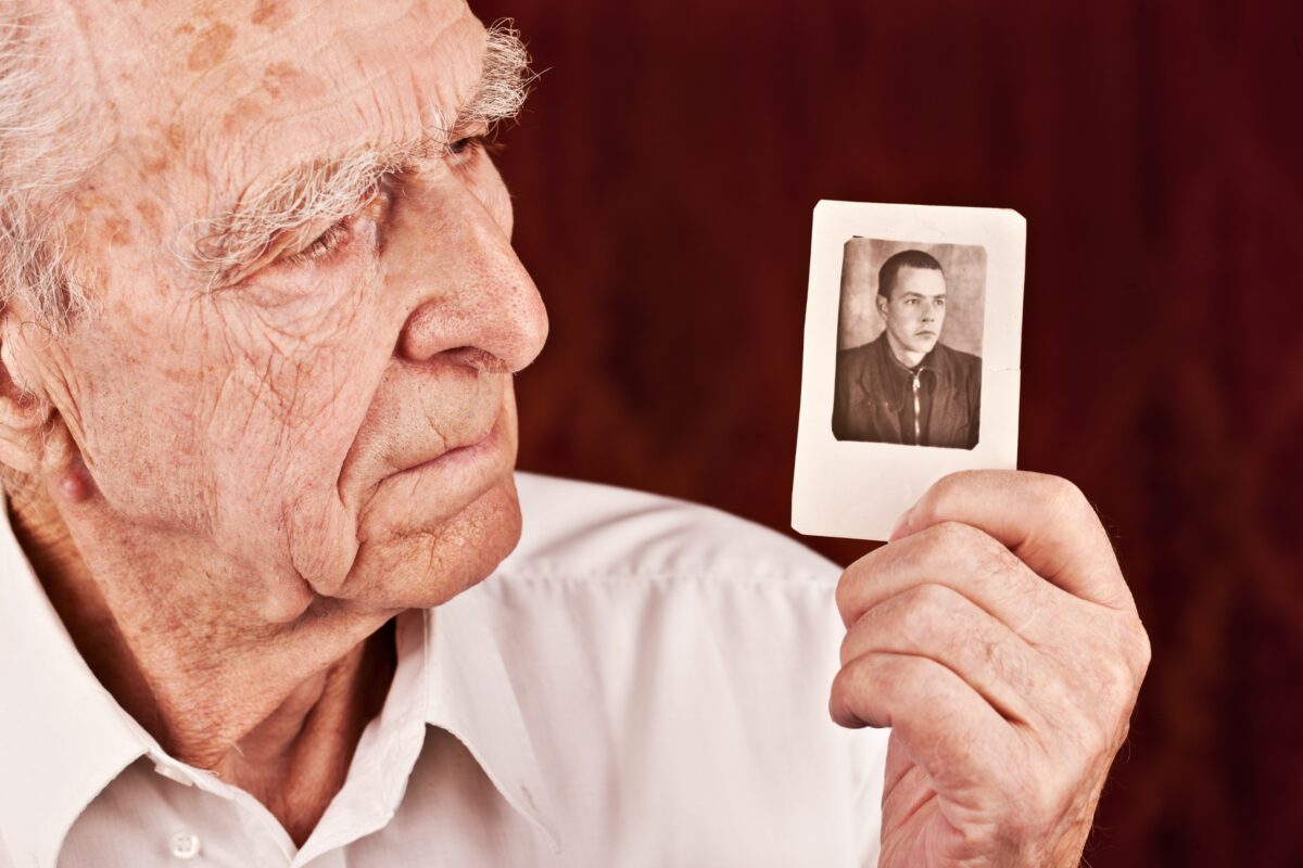 An Elderly Man Is Showcasing The Significance Of Photography By Holding Up A Photo Of An Old Man.