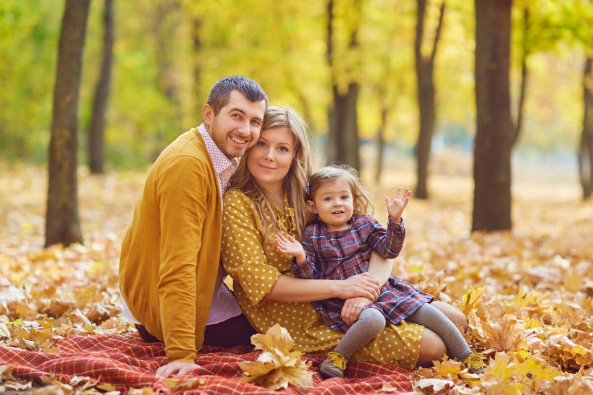 A Family Sitting On A Blanket In An Autumn Park.