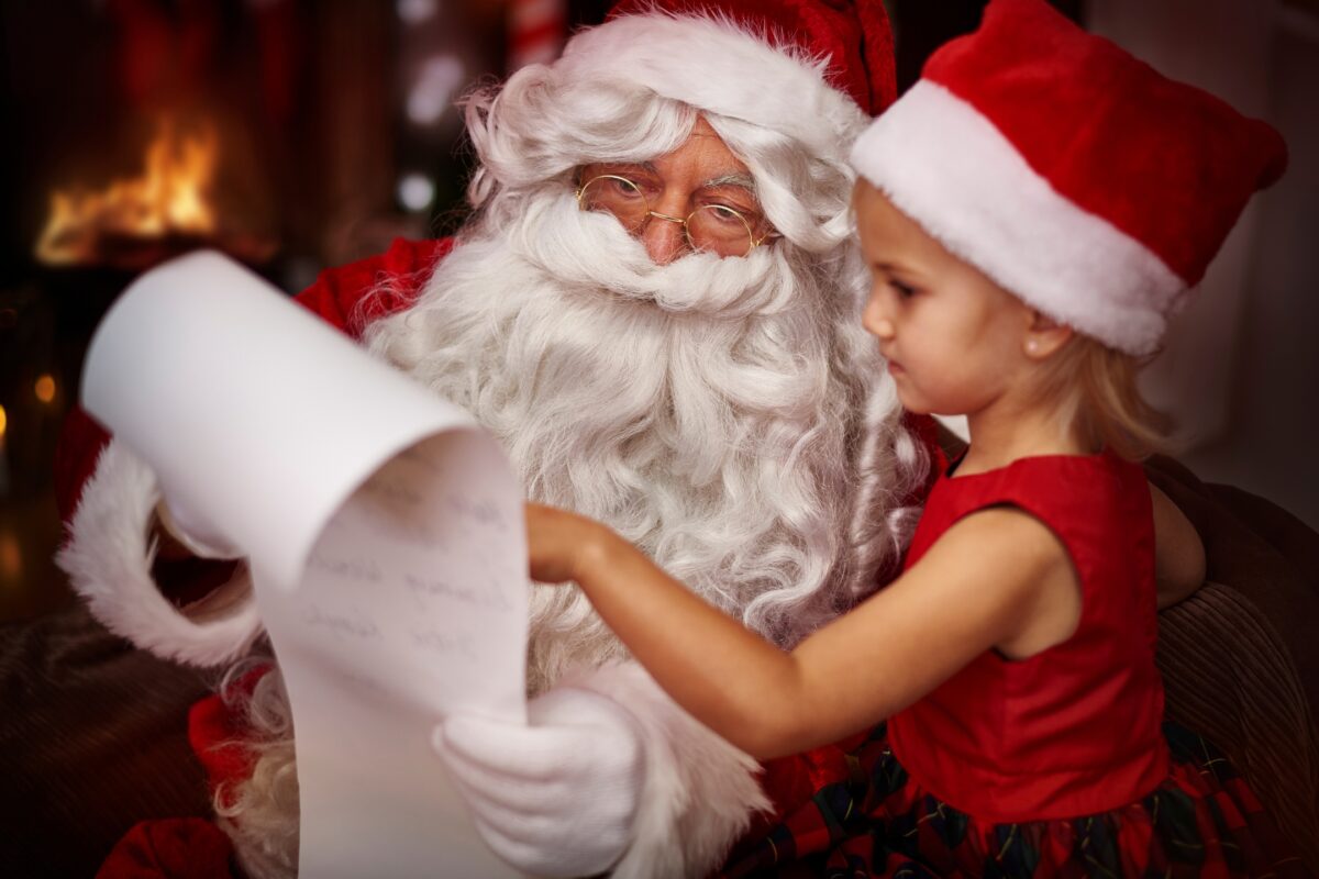 Santa Claus Is Meticulously Dressed In His Iconic Red And White Suit As He Jovially Sits Beside A Young Girl, Attentively Reading Her Heartfelt Letter. This Heartwarming Scene Captures The Essence Of The Santa