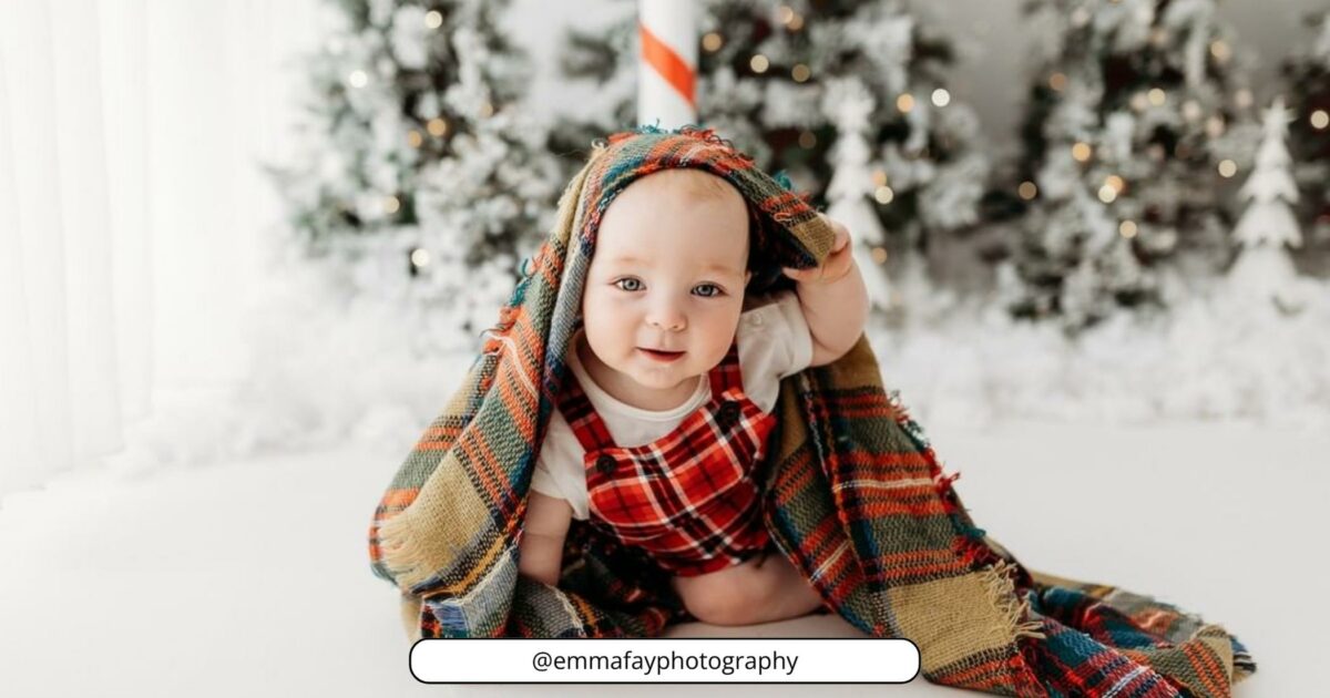 A Baby Wrapped In A Plaid Blanket In Front Of A Christmas Tree.