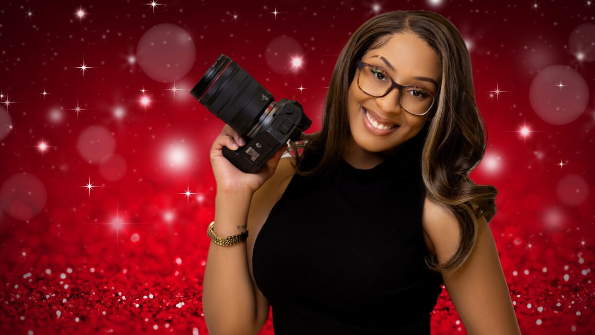 A Woman With Glasses Holding A Camera In Front Of A Red Background, Capturing Captivating Moments During Christmas Mini Sessions.