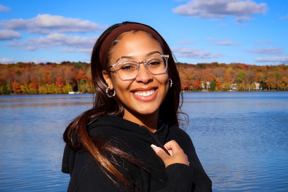 A Woman Wearing Glasses And A Hoodie In Front Of A Lake.