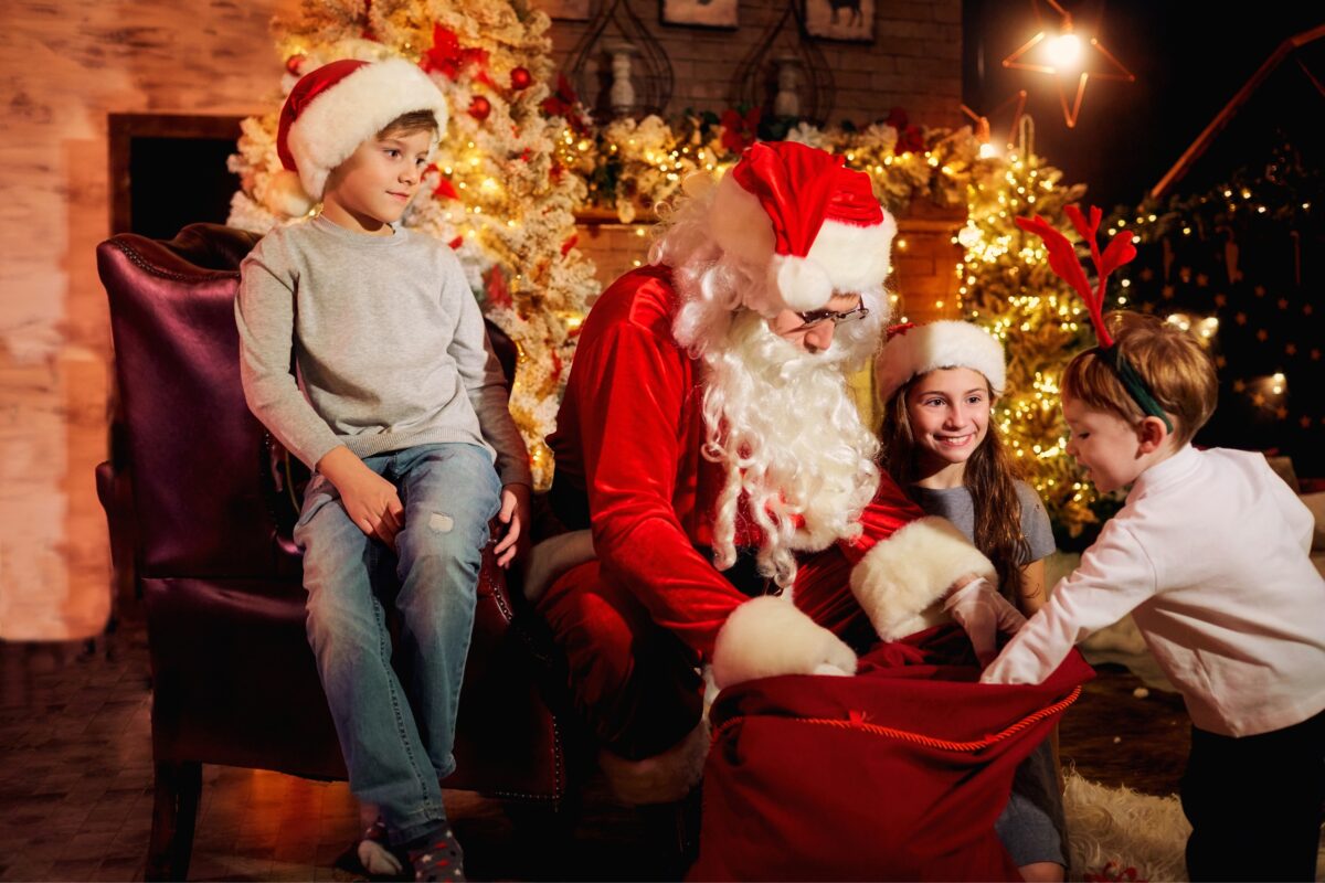 Children Excitedly Engage In Santa Mini Sessions In Front Of A Beautifully Decorated Christmas Tree.