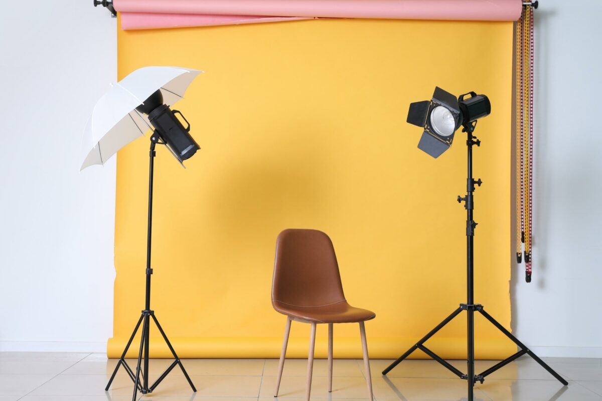 A Chair, Umbrella, And Lighting Equipment Set Up In Front Of A Yellow Backdrop.