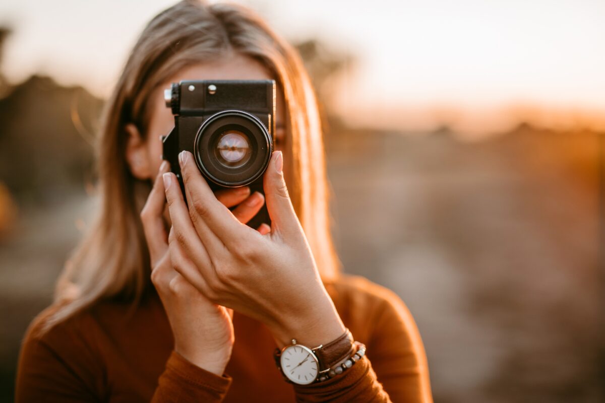 A Woman Is Taking A Picture With Her Camera At Sunset.