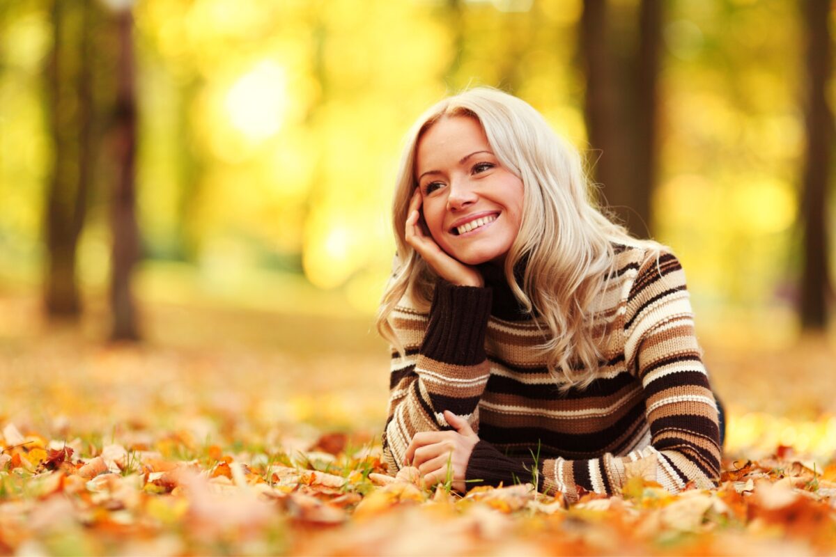 A Woman Is Laying On The Ground In An Autumn Park.