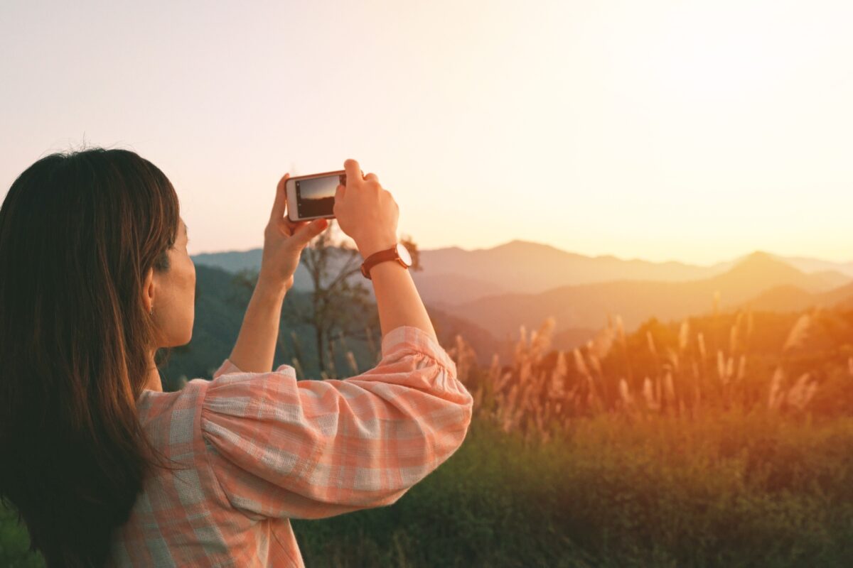 A Woman Is Capturing A Stunning Mountain Vista With Her Cell Phone Using Mobile Photography Tips.