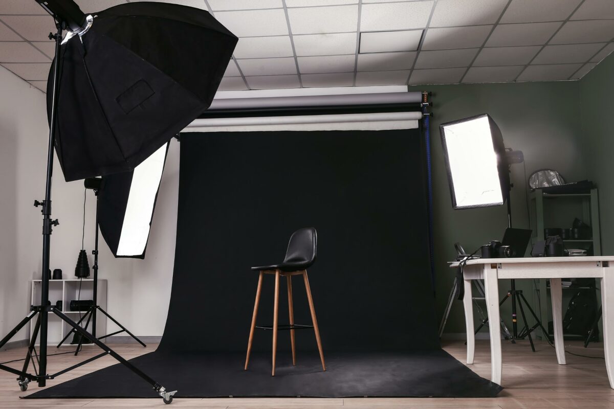 A Photo Studio With A Modern Black Background And A Sleek Black Chair, Showcasing Expert Lighting Techniques.