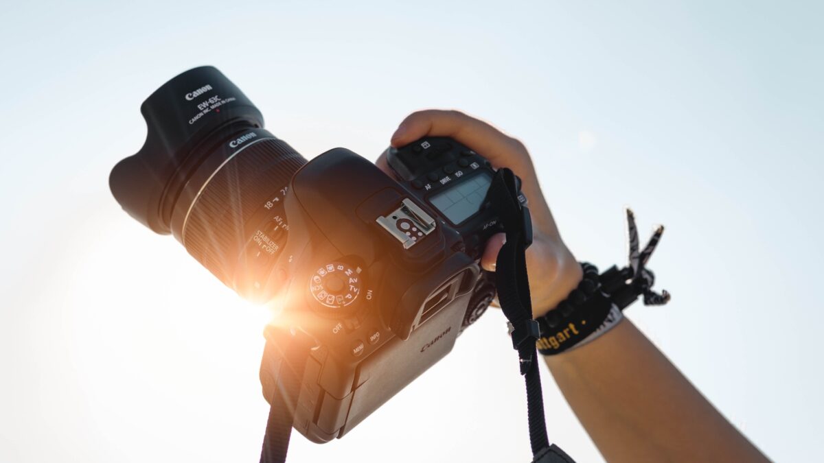 A Person Holding A Dslr Camera With The Sun Behind It, Capturing Moments And Learning From Mistakes As A Photographer.