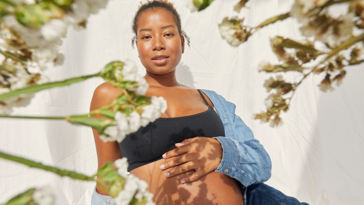 A Perfect Pregnant Woman Posing In Front Of Flowers For Indoor Photos.