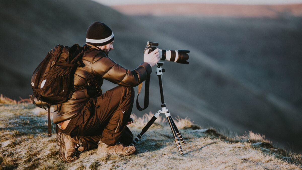 A Man Holding A Camera On Top Of A Mountain, Learning From His Mistakes As A Photographer.