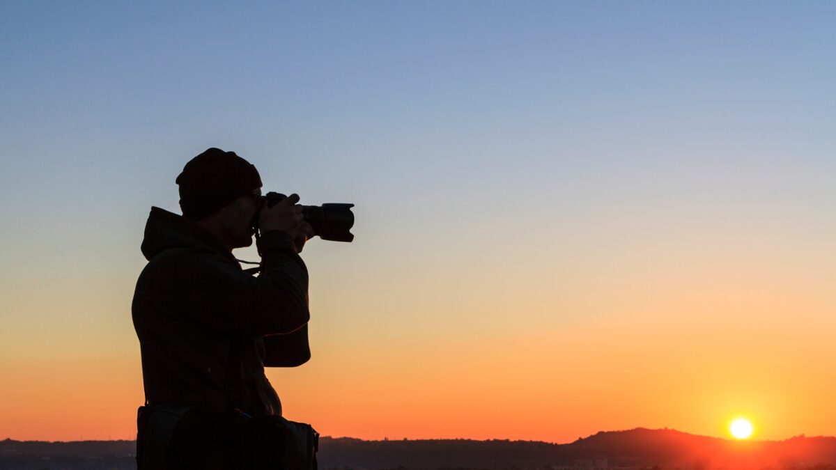 A Silhouette Of A Man Taking A Photo At Sunset.